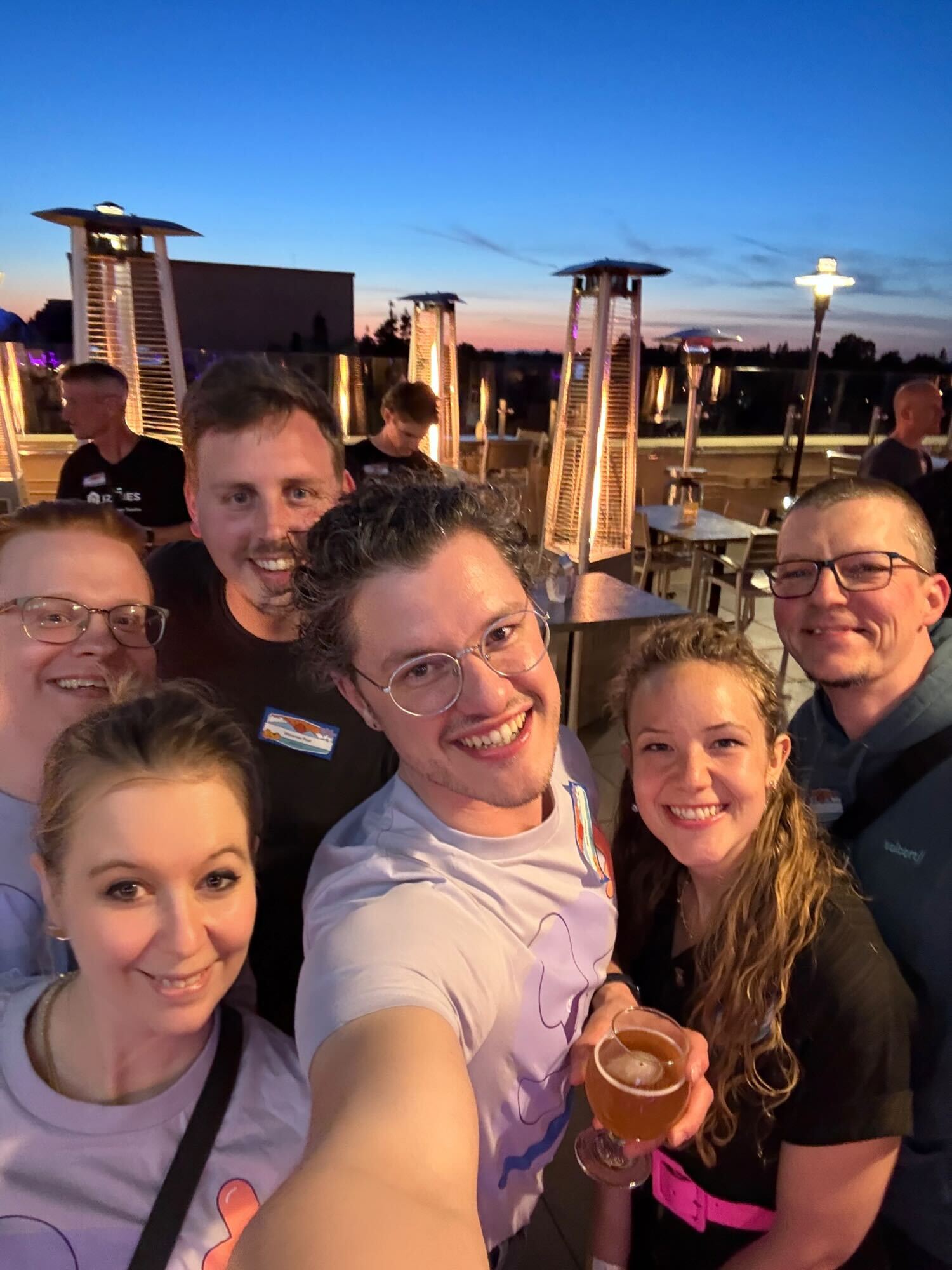 A group of five smiling team members taking a selfie at the K15t Hocketse rooftop social event during sunset.